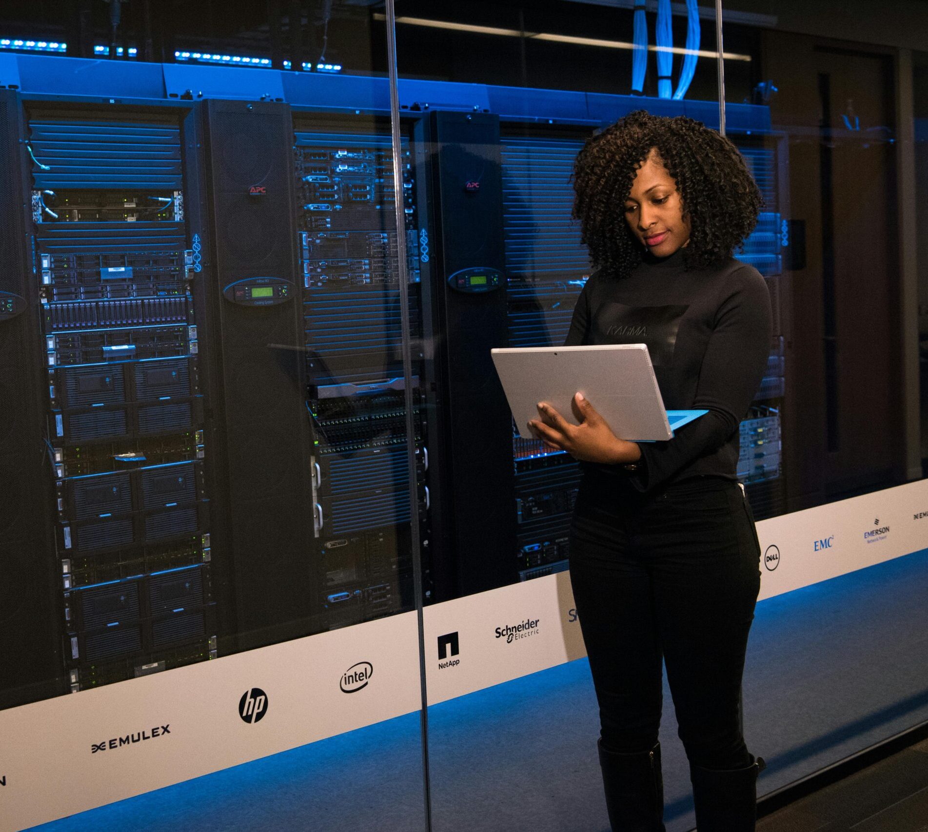 A female engineer using a laptop while monitoring data servers in a modern server room.